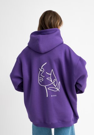 Haut à capuche violet surdimensionné avec un dessin contour d'un visage et d'une feuille au dos. Le tissu a une texture lisse ; il dispose d'une grande capuche.