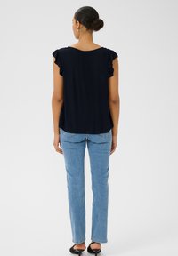 Blouse bleu marine avec des manches à volants, associée à un jean bleu clair. Tissu doux et coupe ample, avec un col arrondi et un détail au dos.