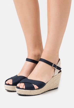 Navy fabric wedge sandals with an espadrille jute sole, open toe, cross-over straps, and ankle strap featuring a gold buckle detail.