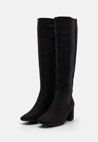 Bottes noires montantes en daim doux, avec un bout pointu, un talon épais et des panneaux élastiques sur les côtés pour une silhouette ajustée.
