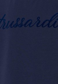 Maglietta blu navy con una superficie liscia, caratterizzata da testo in corsivo blu scuro lucido "Trussardi" centrato sul tessuto.
