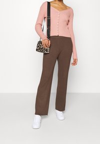 Jasnoróżowy, prążkowany kardigan na długi rękaw z guzikami, w zestawie z brązowymi dopasowanymi spodniami i białymi trampkami. Mała torebka w panterkę.