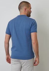 Modrá polo košile z texturované tkaniny, s krátkým límcem a krátkými rukávy. Střih je přizpůsobený a má jednobarevný design.