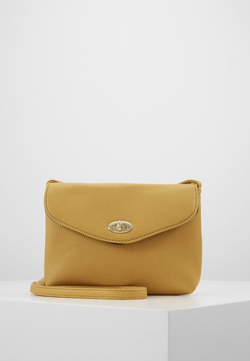 Żółta skórzana torba na ramię z teksturowaną powierzchnią, klapką zamykającą i złotymi akcentami metalowymi. Zawiera odpinany pasek.