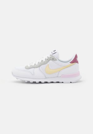 Biało-szary sneaker Nike z żółwym znakiem, różowym akcentem na podeszwie i bordową zakładką na pięcie, pokazany z profilu na białym tle.