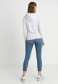 Sudadera gris con capucha forrada, combinada con jeans ajustados azules y zapatillas ligeras de color azul. Diseño sencillo, con puños y cinturilla acanalados.