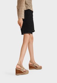 Sandali con zeppa a fascette in tessuto intrecciato, con tomaia color beige chiaro, base marrone scuro e dettaglio della suola intrecciato.