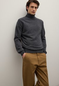 Maglione dolcevita grigio in morbido tessuto a maglia, abbinato a pantaloni color sabbia. Il maglione presenta una silhouette aderente e polsini a coste.