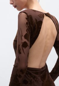 Pruun lilletrükiga kleit kõrge kaelusega ja pikkade läbipaistvate varrukatega. Omaduseks on avatud seljatoega disain ja sile tekstuur.