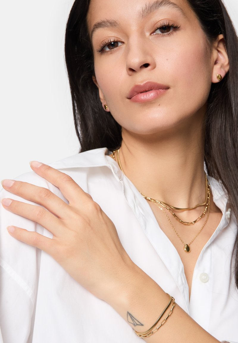 Set di gioielli in tonalità oro che comprende collane a strati, un pendente e un bracciale. Texture liscia con una combinazione di stili di catena e finiture lucide.