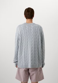 Übergroßer hellblauer Strickpullover mit Rippbund und -bündchen. Verfügt über ein strukturiertes Muster; getragen mit rosa Shorts, Ansicht von hinten.