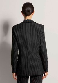 Schwarzer und weißer Blazer mit Nadelstreifen, mit Reverskragen, strukturierten Schultern und Knopfmanschetten in Dreifachausführung. Maßgeschneiderte Passform und glatter Stoff.