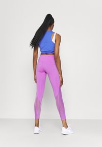 Top atlético sin mangas de color azul con perforaciones, combinado con leggins rosas que tienen paneles de malla; zapatillas blancas completan el atuendo.
