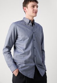 Button-up shirt in a dark blue denim fabric. Features a spread collar, long sleeves, and contrasting buttons. Smooth texture, casual fit.