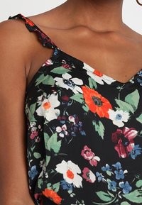 Mustapohjainen spagettiolkaiminen paita, jossa on värikkäitä kukkia punaisena, valkoisena ja sinisenä vihreiden lehtien kanssa; herkät röyhelöolkain.