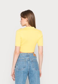 Top cropped amarelo canelado com mangas curtas; combinado com jeans de cintura alta azul claro com bolsos de remendo e um rótulo de couro na parte de trás.