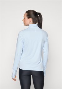 Ljusblå långärmad topp med hög krage, med en subtil detalj på baksidan och figursydd design, som kombineras med svarta leggings.
