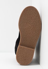 Svart mockaboot med en strukturerad gummisula. Sulan är ljusbrun och har ett lätt upphöjt mönster för grepp.