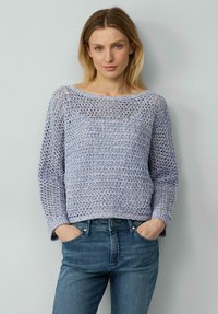 Helles blaues, gestricktes Sweatshirt mit lockerem Häkelmuster, weitem Ausschnitt und langen Ärmeln. Kombiniert mit dunkelblauen Jeans.