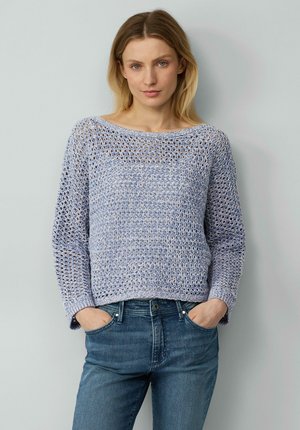 Helles blaues, gestricktes Sweatshirt mit lockerem Häkelmuster, weitem Ausschnitt und langen Ärmeln. Kombiniert mit dunkelblauen Jeans.