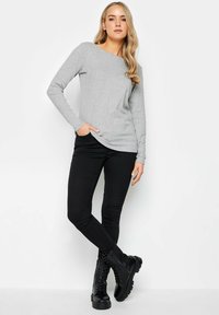 Graues Langarmoberteil mit einem Boot-Ausschnitt, kombiniert mit schwarzen Skinny-Jeans und schwarzen Schnürstiefeln mit einer klobigen Sohle.