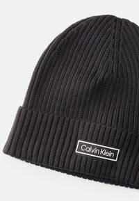 Czarna, prążkowana czapka beanie z podwini�ętym mankietem, z prostokątną naszywką z logiem Calvin Klein w białym i czarnym kolorze.