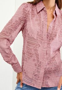 Light pink sheer button-up shirt with textured leaf patterns and subtle stripes, featuring a collar and long sleeves.