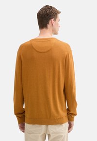 Suéter de punto color mostaza con cuello redondo, mangas largas y un corte relajado. Cuenta con puños y dobladillo acanalados, textura suave.