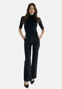 Sort tætsiddende turtleneck-top, kombineret med højtaljede, sorte, udvidede bukser. Outfitet har en glat tekstur og et minimalistisk design, suppleret med skinnende sorte hæle.