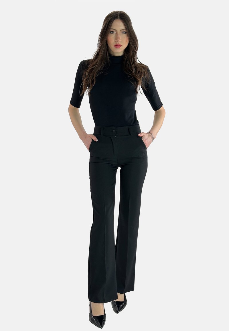 Maglione collo alto nero e pantaloni neri a palazzo sartoriali. L'outfit presenta una texture liscia e una silhouette aderente con tasche.