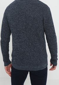 Dark blue knitted sweater with a textured pattern, round neckline, long sleeves, and a slightly longer back hem. Casual fit.