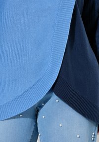 Modrý a námořnický pletený svetr s ribbed zakončením, vrstvovým designem, vyznačující se hladkou texturou. V kombinaci s modrými džíny ozdobenými perlami.