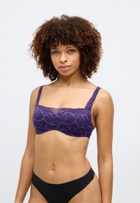 Violet mežģīņu bralette ar ziedu rakstiem, platām mežģīņu siksnām un gludu apakšmalu. Saskaņota ar melniem apakšbiksēm.