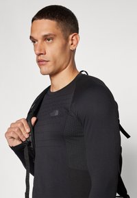 Schwarzes, langärmliges Sportshirt mit strukturierten Einsätzen und tailliertem Design. Mit dem North Face-Logo auf der Brust und verstellbaren Schulterträgern.