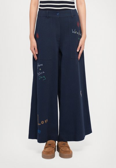 Φαρδιά μπλε παν trousers με πολλές τσέπες, διαθέτουν πολύχρωμες κεντητές φράσεις. Μαλακό, υφή ύφασμα με άνετη εφαρμογή.