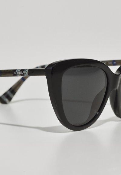 Black sunglasses with a chunky cat-eye frame, featuring dark lenses and a patterned temple. The brand logo "Burberry" is visible on the side.