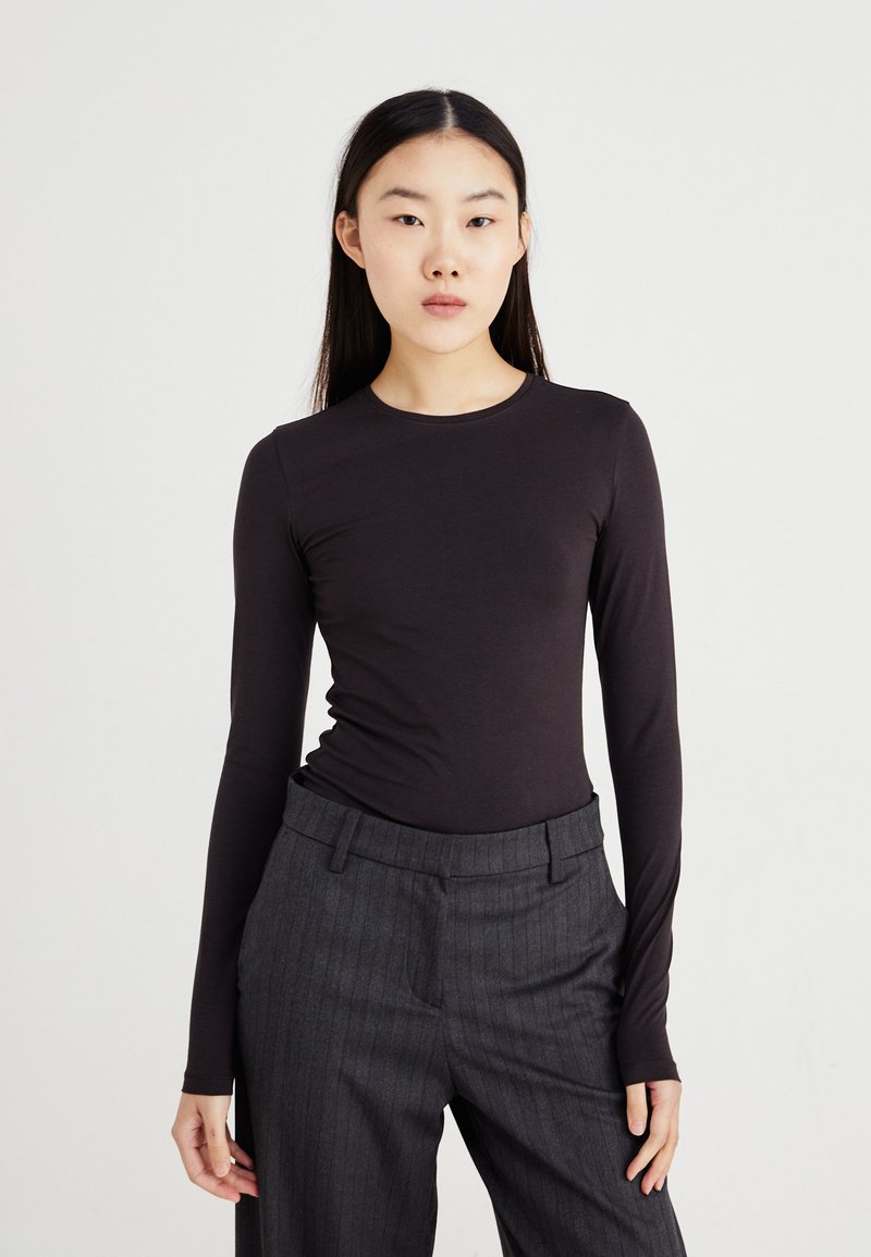 Bluză neagră cu mânecă lungă, fabricată dintr-un material elastic, cu decolteu rotund și design ajustat, asortată cu pantaloni gri cu dungi subțiri.