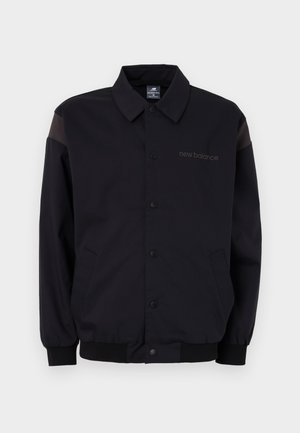 Zwarte jas met een knoopsluiting aan de voorkant, ribbelmanchetten en kraag. Heeft contrasterende schouderpanelen en een logo op de borst. Soepele textuur.