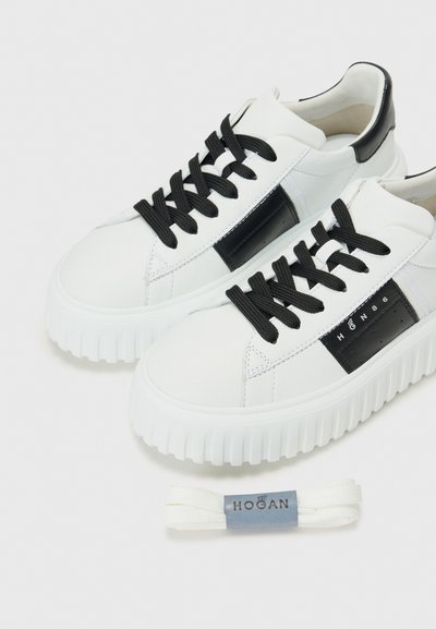 Baskets blanches avec des lacets noirs et un panneau latéral. Semelle épaisse avec texture nervurée. Comprend des lacets blancs supplémentaires étiquetés "HOGAN."
