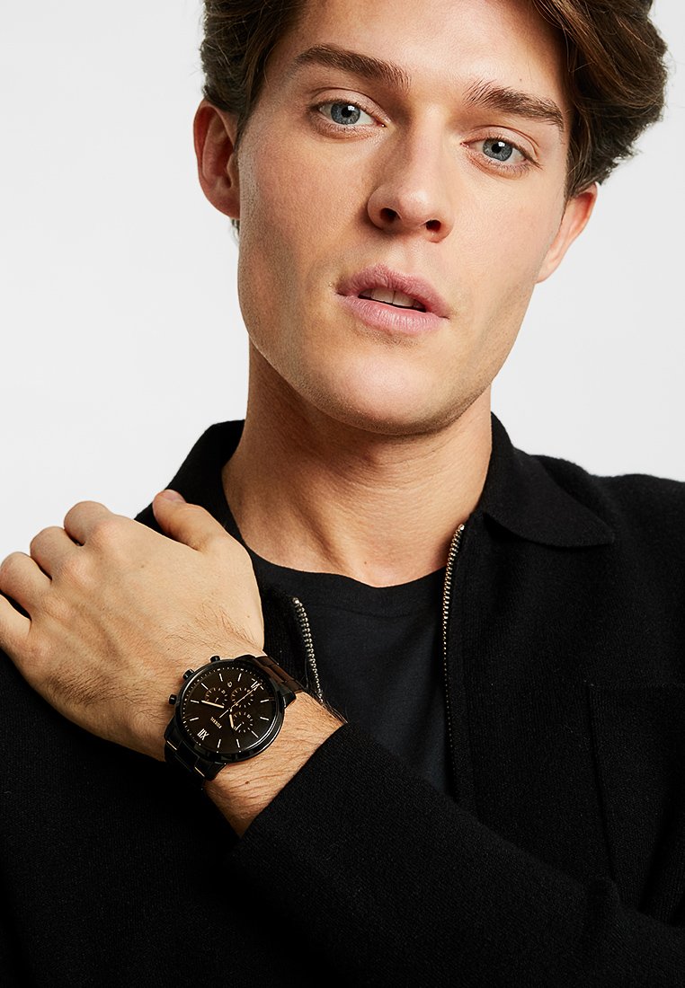 Montre chronographe noire avec un boîtier rond et un cadran noir. Dispose de marqueurs d'heure blancs et d'un bracelet noir lisse et texturé.