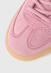 Ροζ σουέντ αθλητικό παπούτσι με υφασμάτινο πάνω μέρος, αντίθετη ροζ ραφή κ αι σόλα από καουτσούκ χρώματος τσίχλας. Ο σχεδιασμός διαθέτει καμπύλες γραμμές και λεπτομέρειες με κορδόνια.