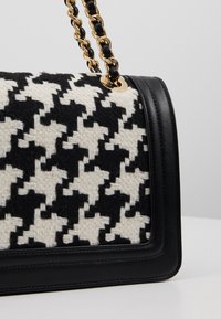 Black and white houndstooth patterned fabric with black leather accents and a gold-chain handle. Rectangular shape with a structured design.