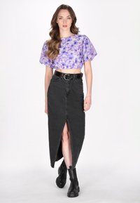 Lilla tie-dye cropped top med pufærmer, parret med en højtaljede sort denim maxiskirt med en frontsplit og sort bælte. Sorte ankelstøvler.