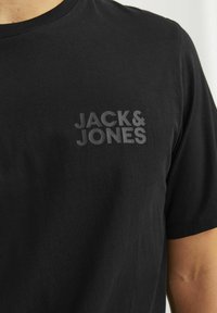 Juodas medvilninis marškinėliai trumpomis rankovėmis, su tonu toną atitinkančiu prekės ženklu "JACK & JONES" krūtinėje. Sklandi tekstūra, klasikinis kirpimas.