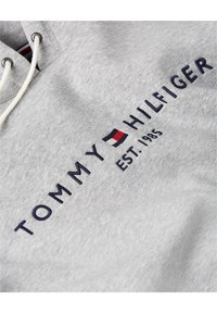 Šedá mikina se stahovací kapucí, s námořnickým modrým vyšitým textem "TOMMY HILFIGER" a "EST. 1985," plus barevným logem.