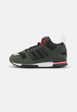 Mørkegrøn og sort Adidas-sneaker med røde hulråb, sorte snørebånd, hvid sål og grønne, røde og sorte stribedetaljer på hælen.