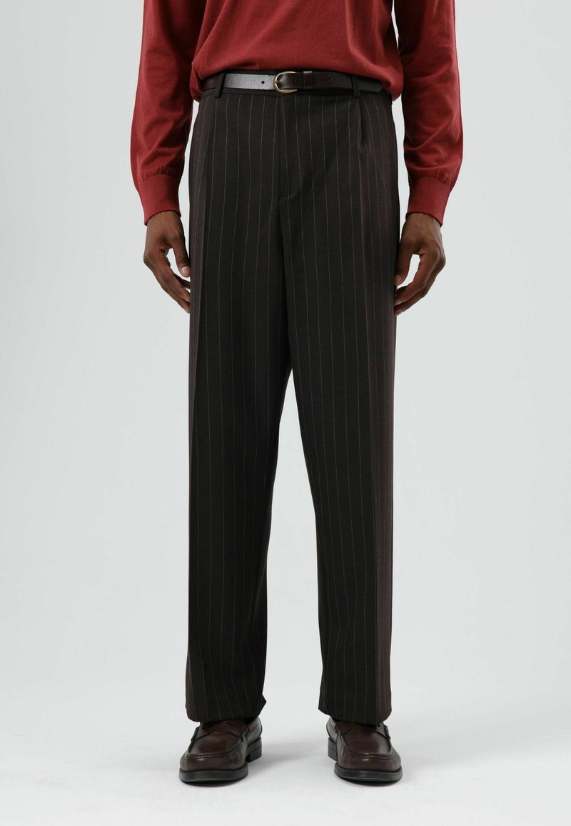 Zwarte broek met krijtstrepen en een losse pasvorm, gemaakt van gestructureerde stof, voorzien van een riem en gedragen met donkere schoenen.