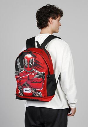 Mochila roja y negra con un gráfico de un personaje enmascarado, con textura suave, cierre de cremallera y correas ajustables y acolchadas.