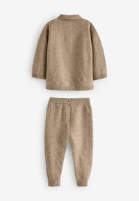 Ensemble pour bébé tricoté beige comprenant un pull et un pantalon. Le pull possède un col côtelé ; le pantalon présente des accents côtelés sur les côtés. Texture douce.