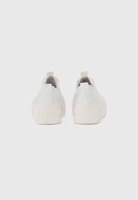 Baskets blanches en toile avec une semelle plateforme texturée, une forme arrondie et une languette au talon pour un enfilage facile.
